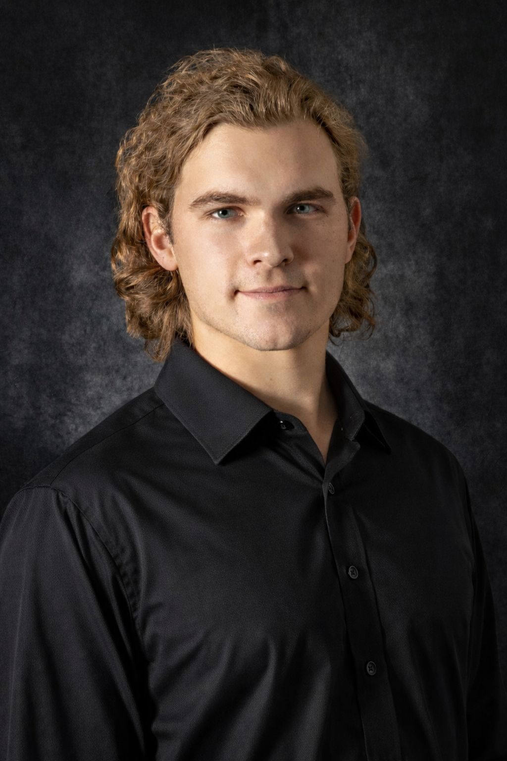A young man with long hair is wearing a blue shirt.