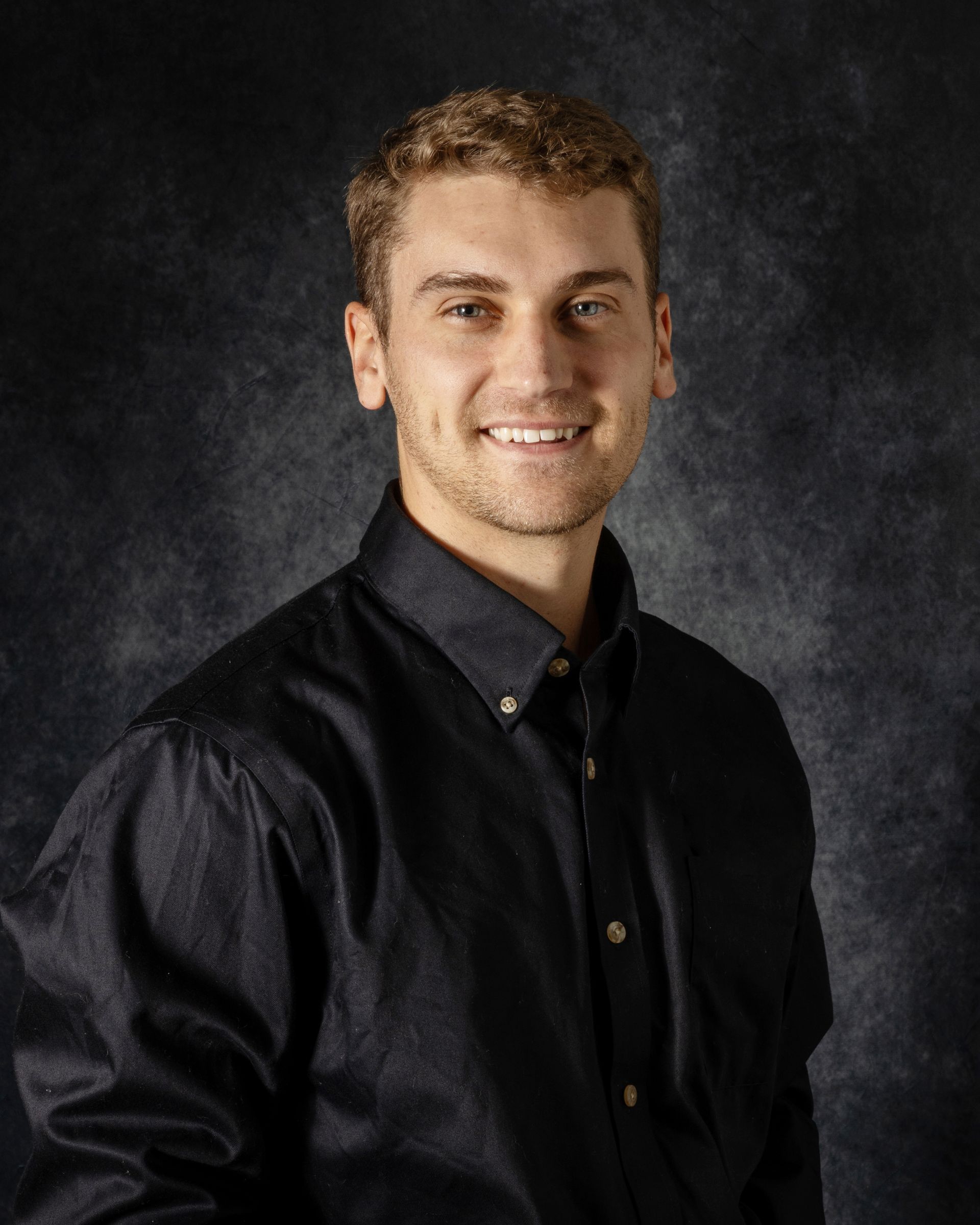 A young man is smiling for a picture in front of a blue background.