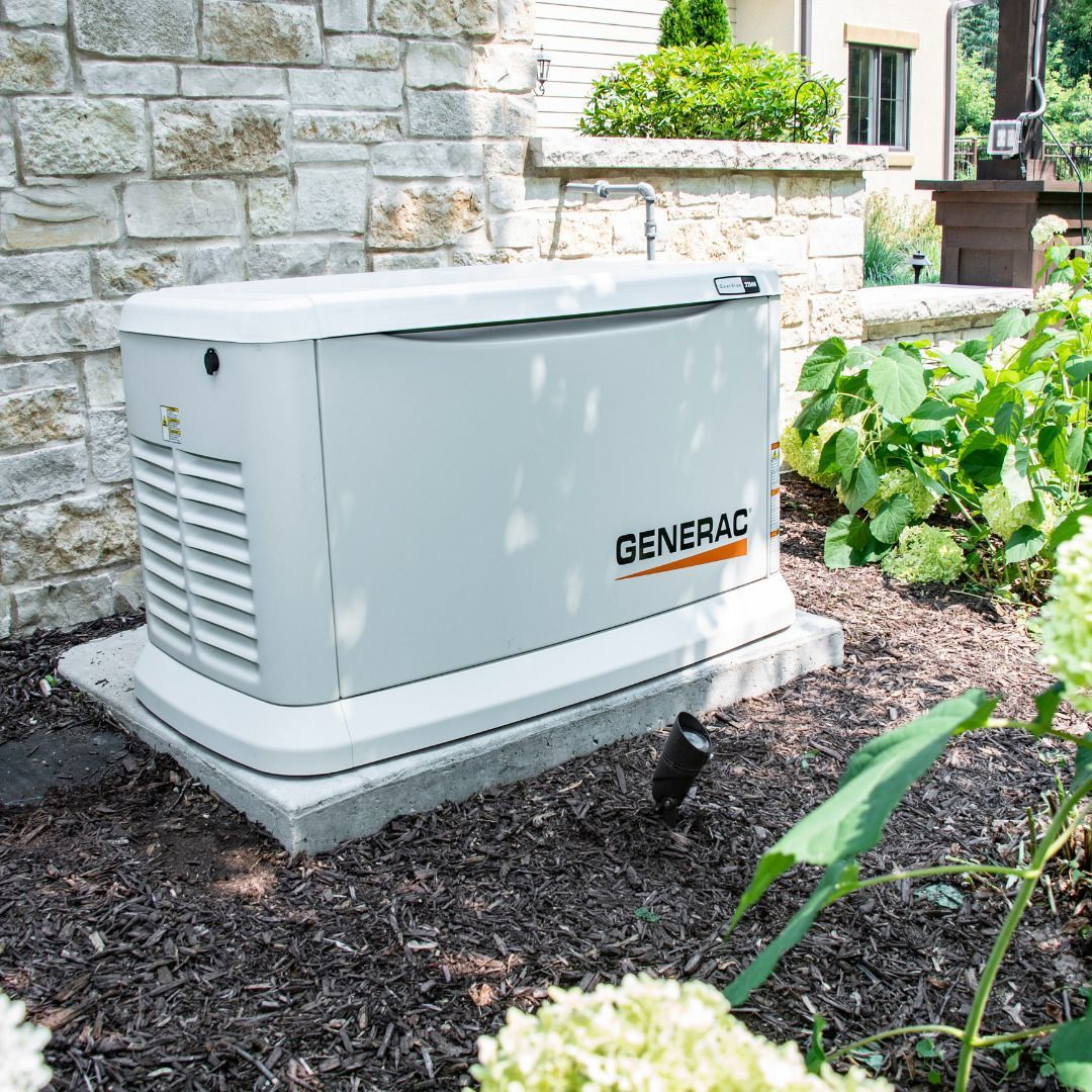 A Generac generator outside a home with tan stone wall and landscaping.