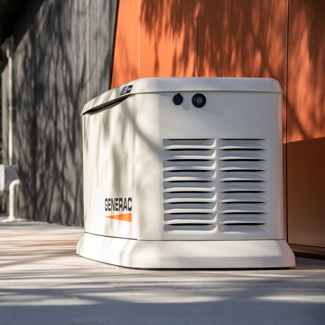 White Generac home backup generator on a concrete pad. Orange wall in background.