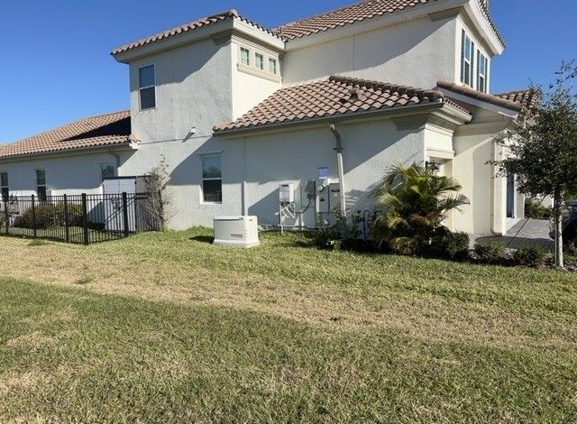Exterior view of a beige house with a tile roof and green grass in front.
