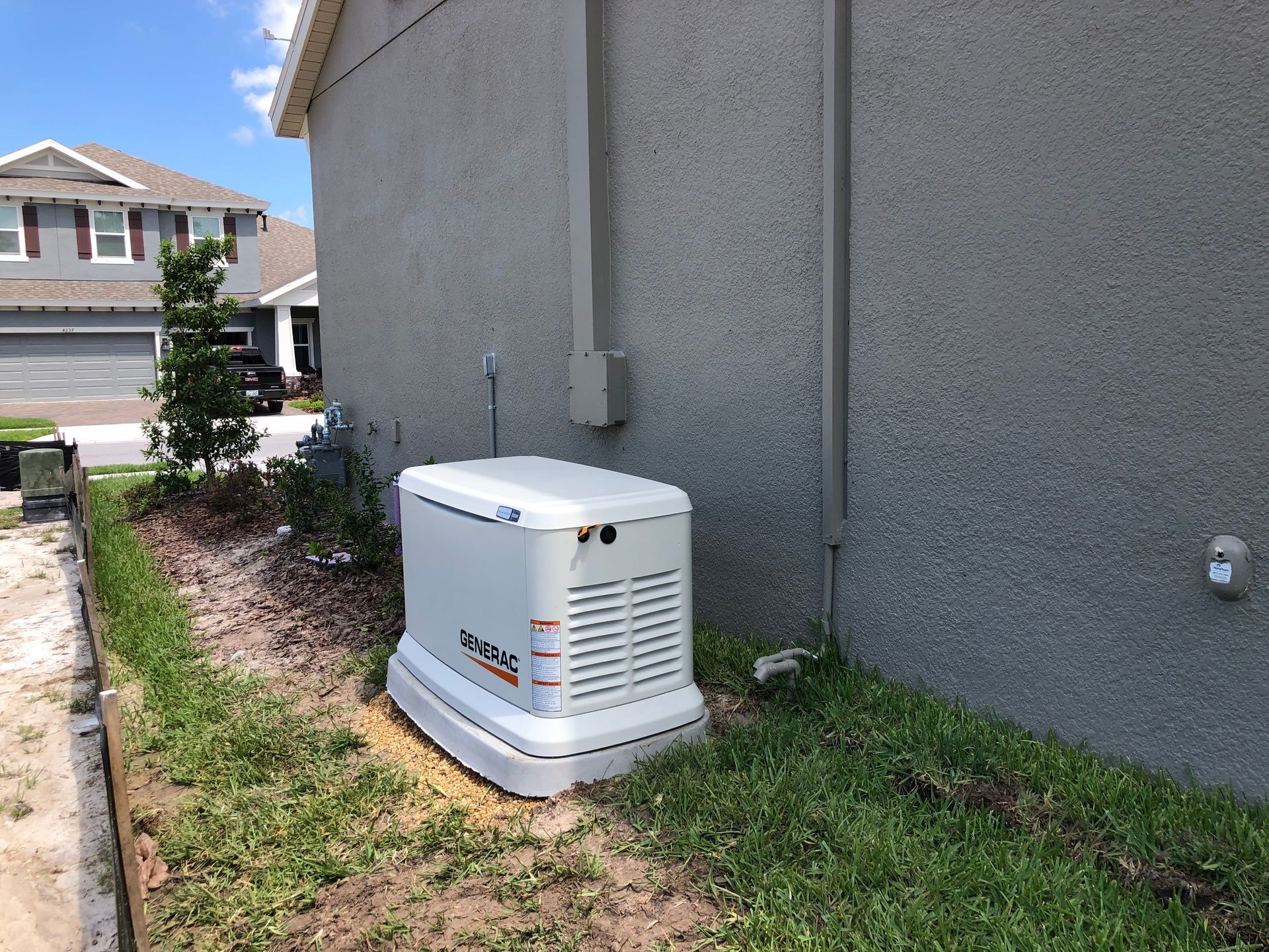 A standby generator sits beside a stucco house. Grass and landscaping are present.