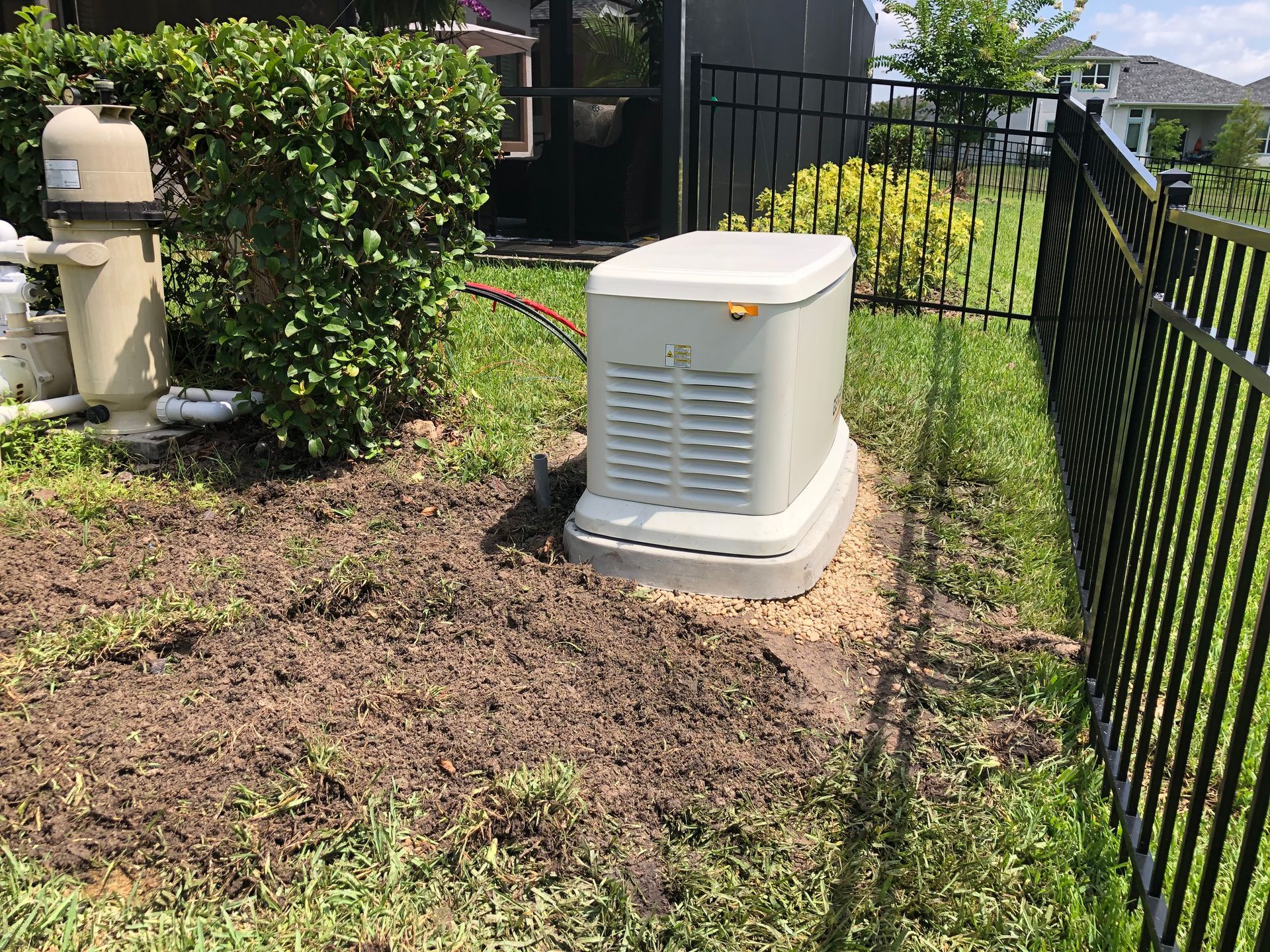 A standby generator next to a black fence, close to a pool area with a brown filter.