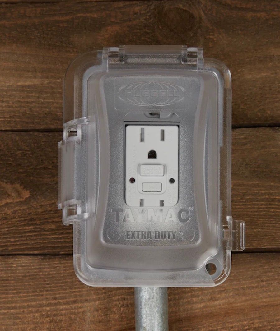 Clear weatherproof electrical outlet cover on a wooden surface.