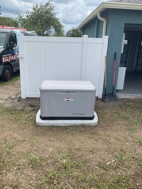 Gray generator on a concrete pad near a white fence and garage. A van is parked to the left.