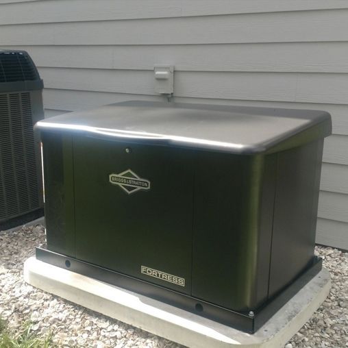 Black Briggs & Stratton home generator on a concrete pad next to a house with gray siding.