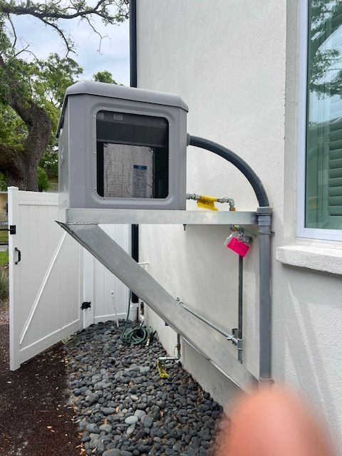 Gray AC unit mounted on metal bracket outside a white stucco building next to a window and fence.