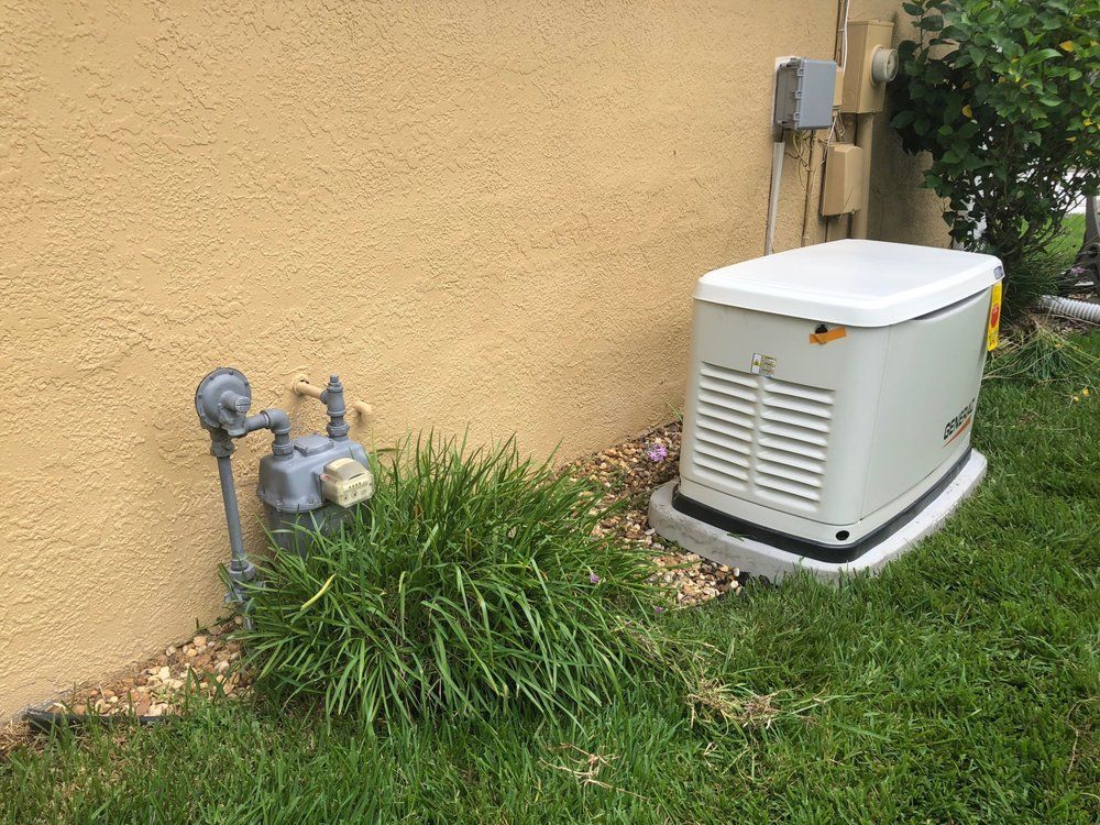 Generator and gas meter next to a stucco wall, surrounded by grass and landscaping.