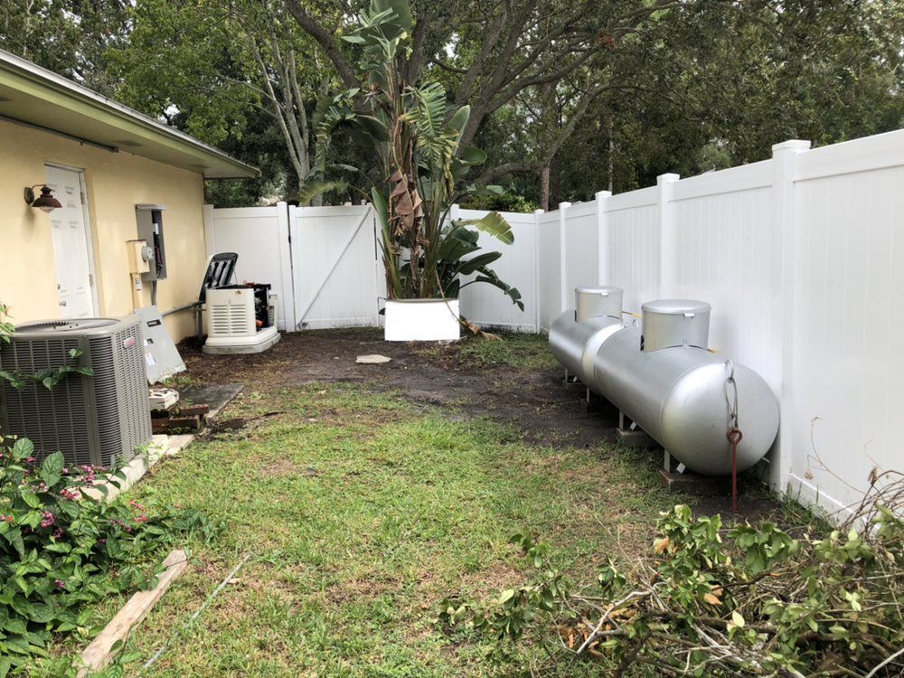 Backyard with HVAC units, propane tanks, white fence, and overgrown grass.