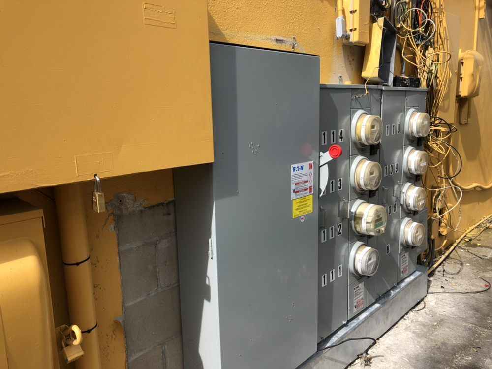 Electrical panel with meters, gray metal box, mounted on a wall; yellow building exterior.