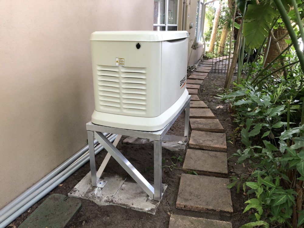 Standby generator on a metal platform beside a house. Stone path and foliage are nearby.