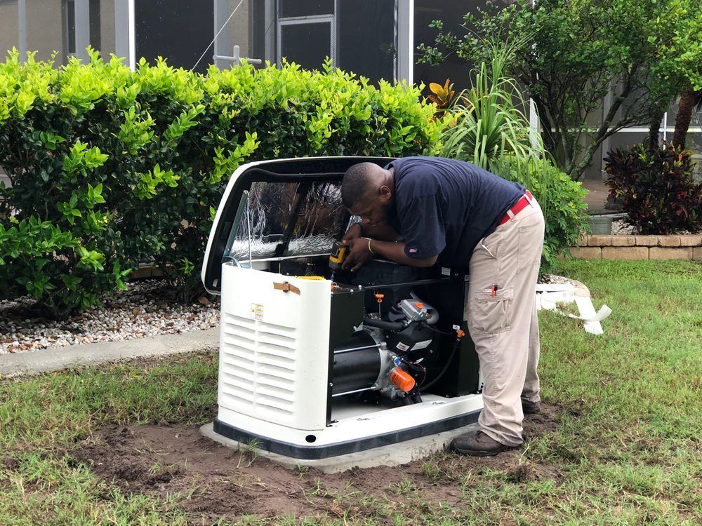 Man servicing a white generator in a yard. He's wearing a blue shirt and tan pants, working with tools.