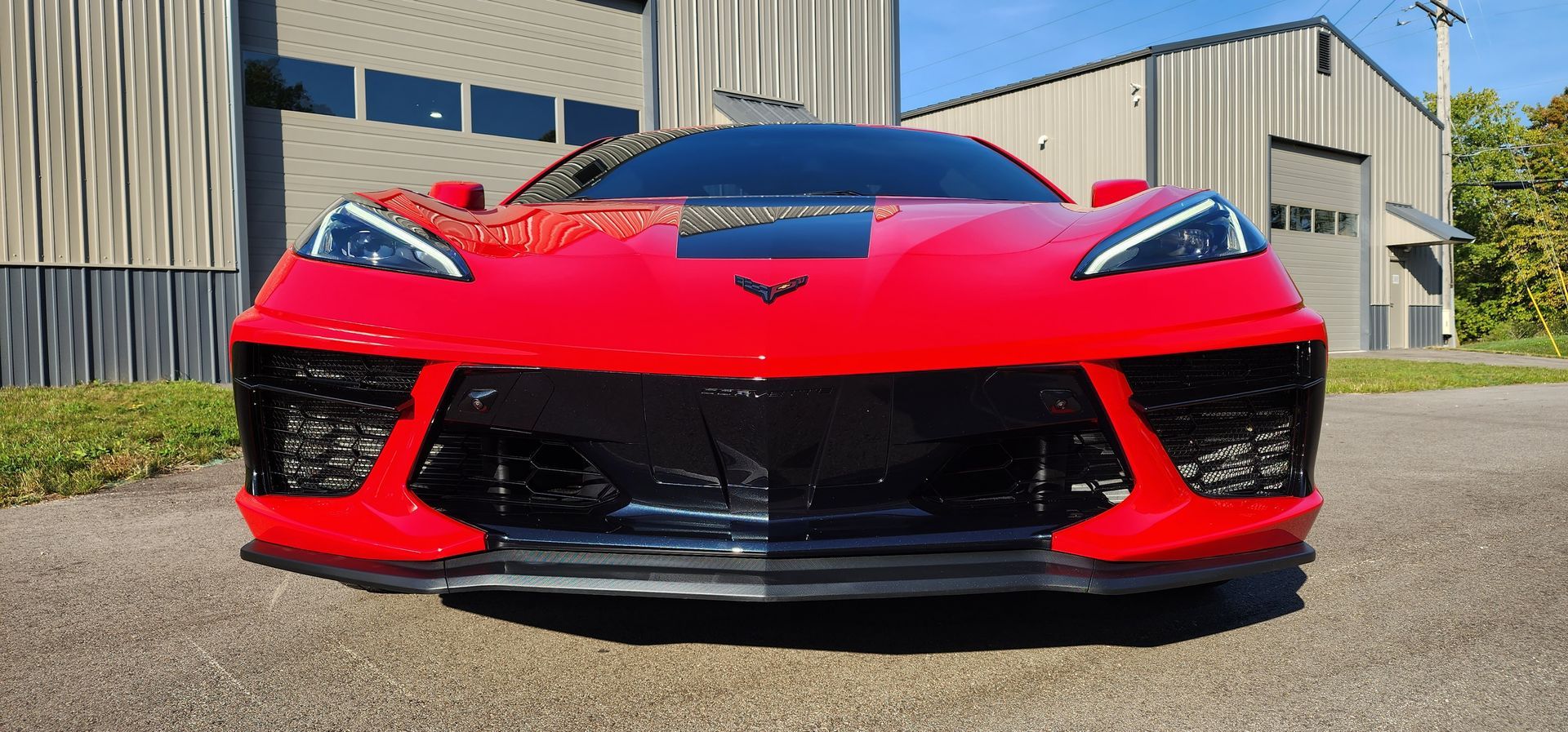 A bright red Chevrolet Corvette sports car parked outdoors in front of a metal building.
