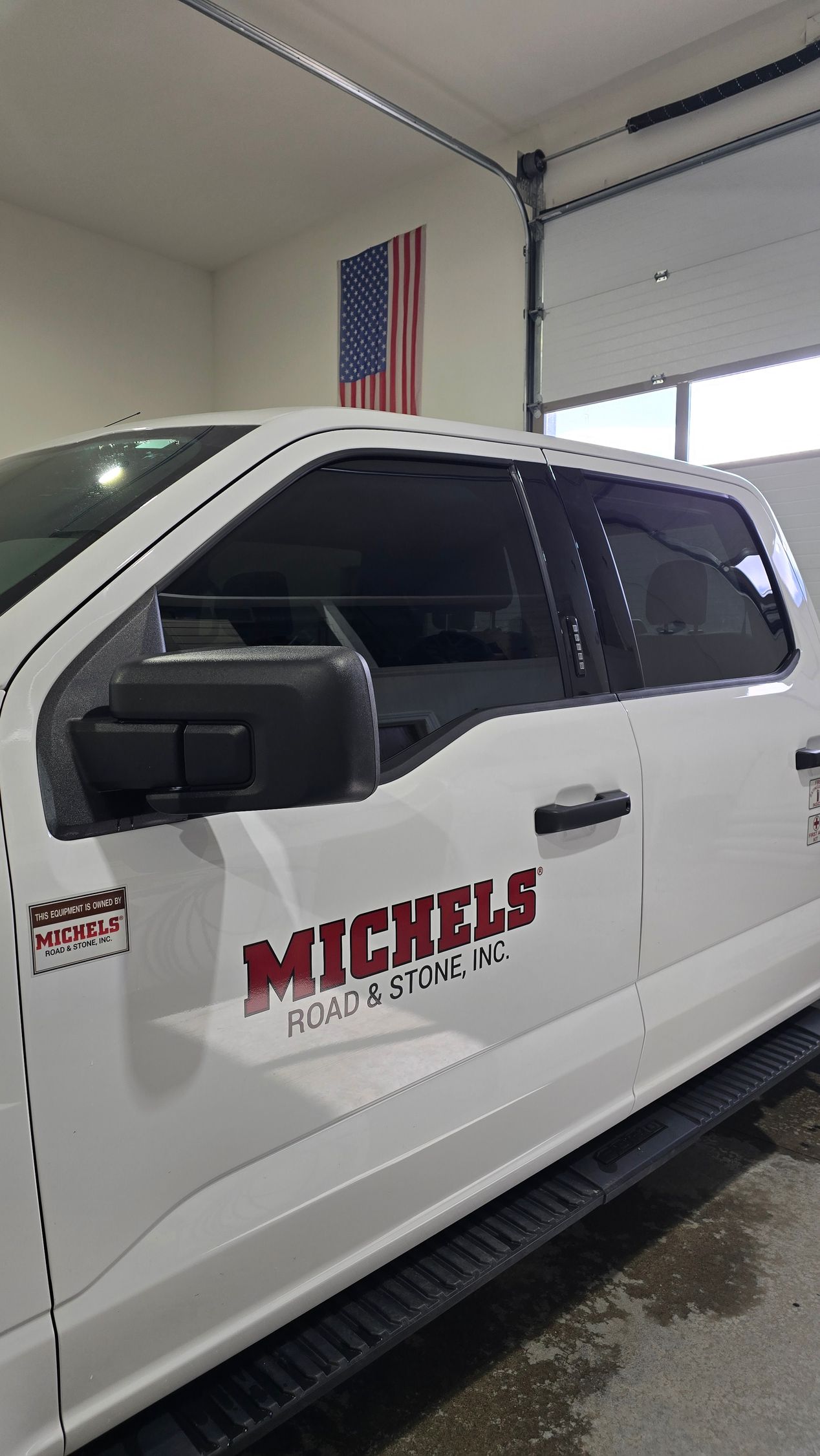 A white pickup truck with the Michels logo on the side, parked in a garage with an American flag on the back wall.