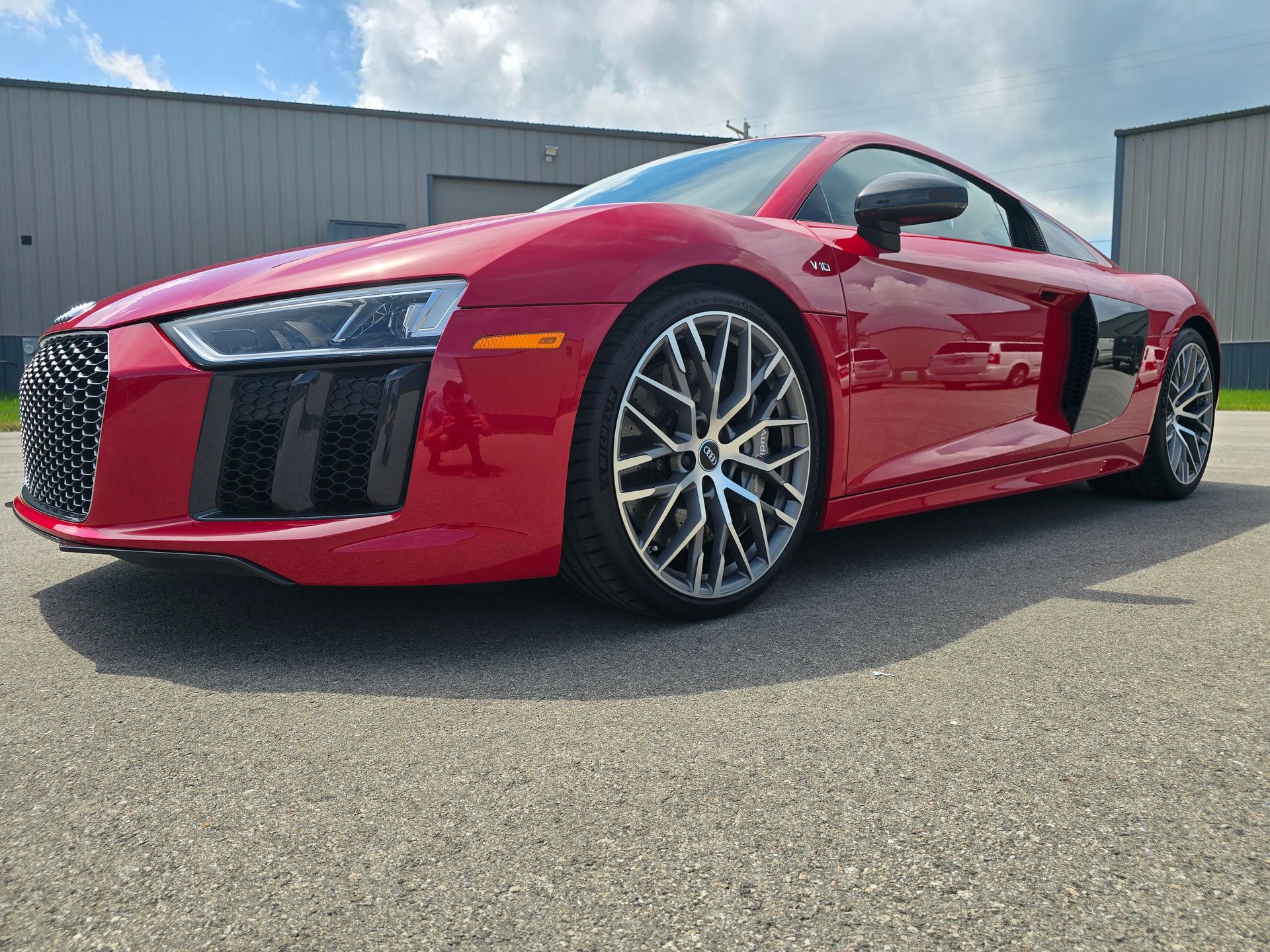 Red Audi R8 sports car parked on asphalt in front of a building on a sunny day.