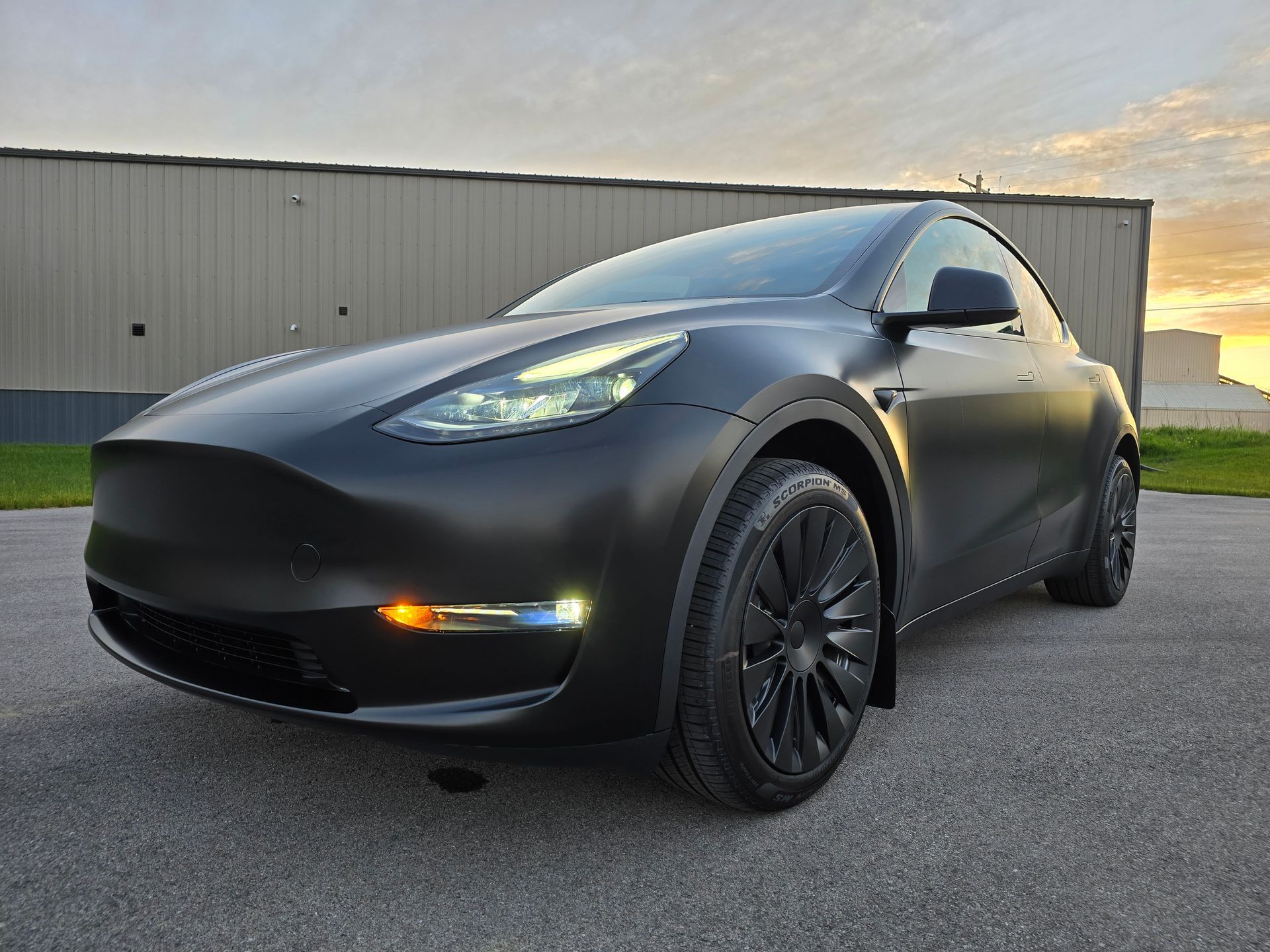 Black Tesla Model Y parked on asphalt in front of a building at dusk.