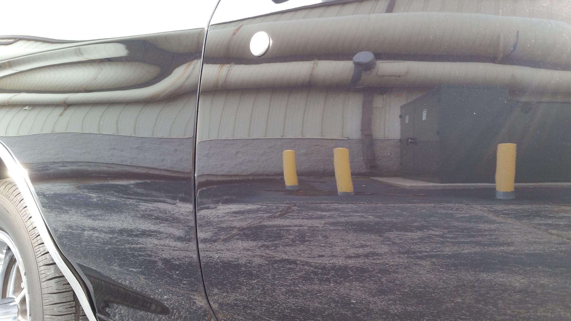 A black car is parked in a parking lot with yellow poles