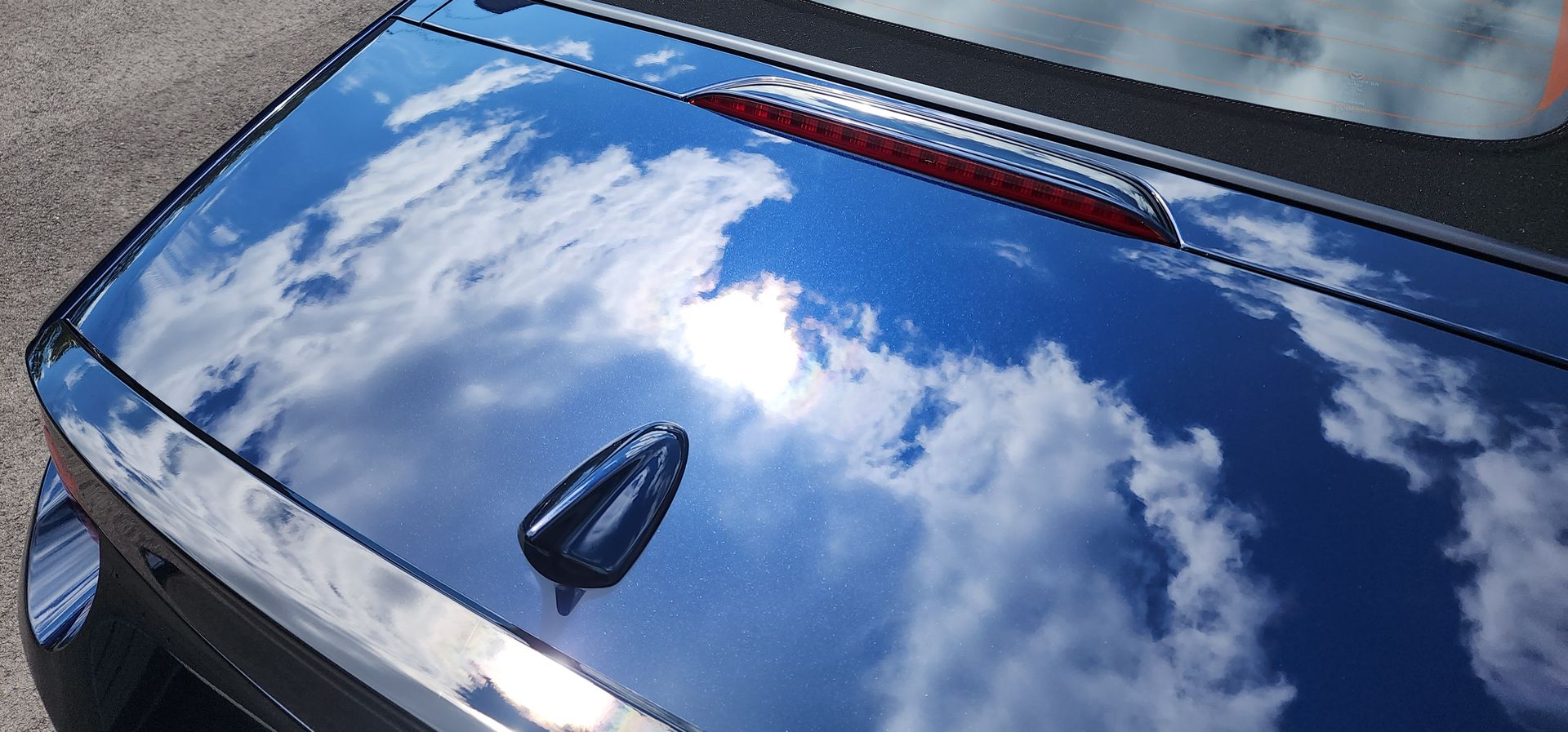 A close up of a blue car with the sky reflected in the hood