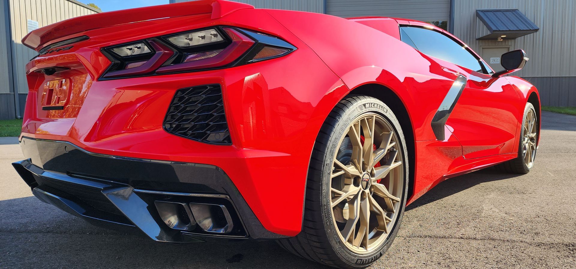 A red sports car with gold wheels is parked in front of a building.