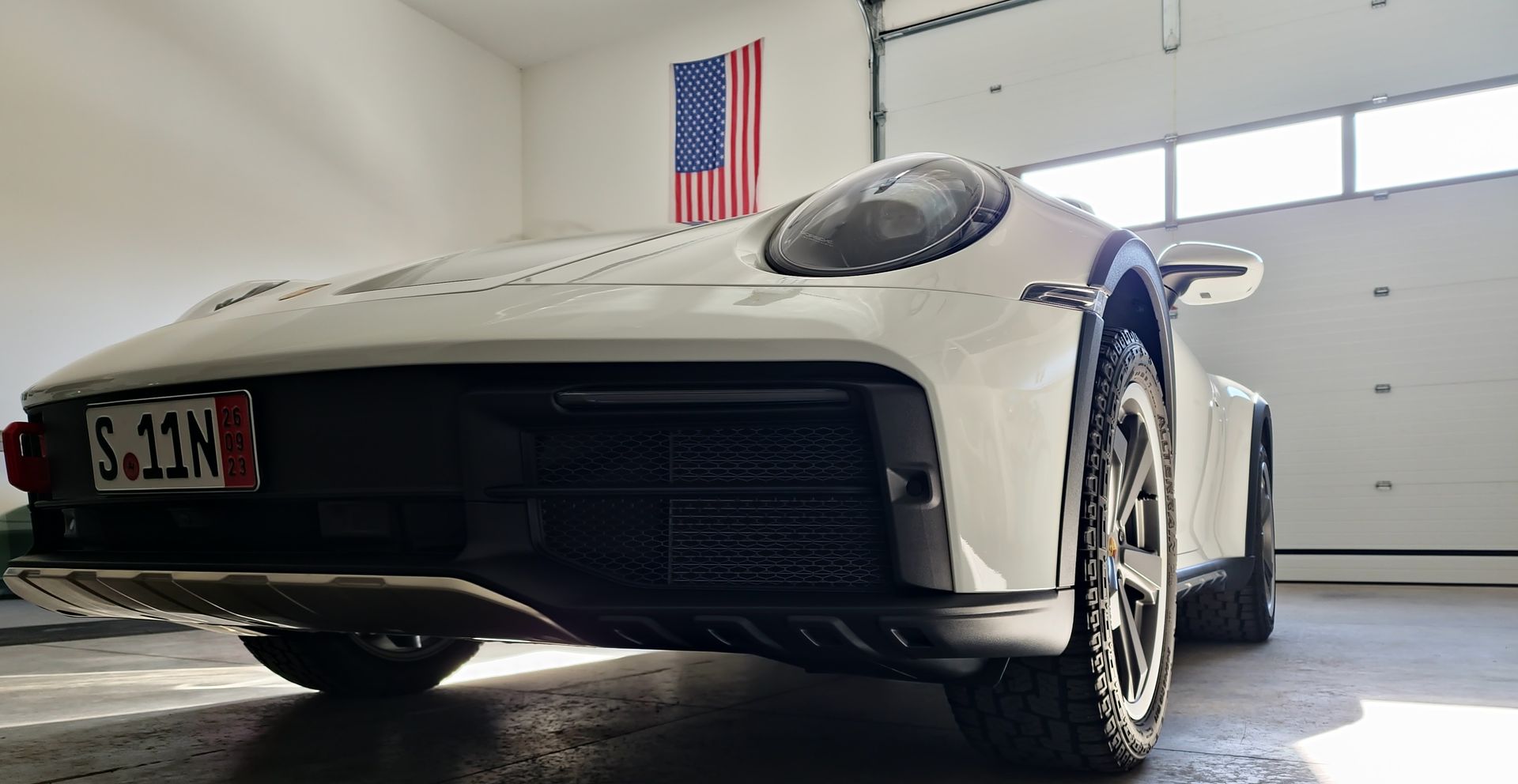 A white sports car is parked in a garage with an american flag on the wall.