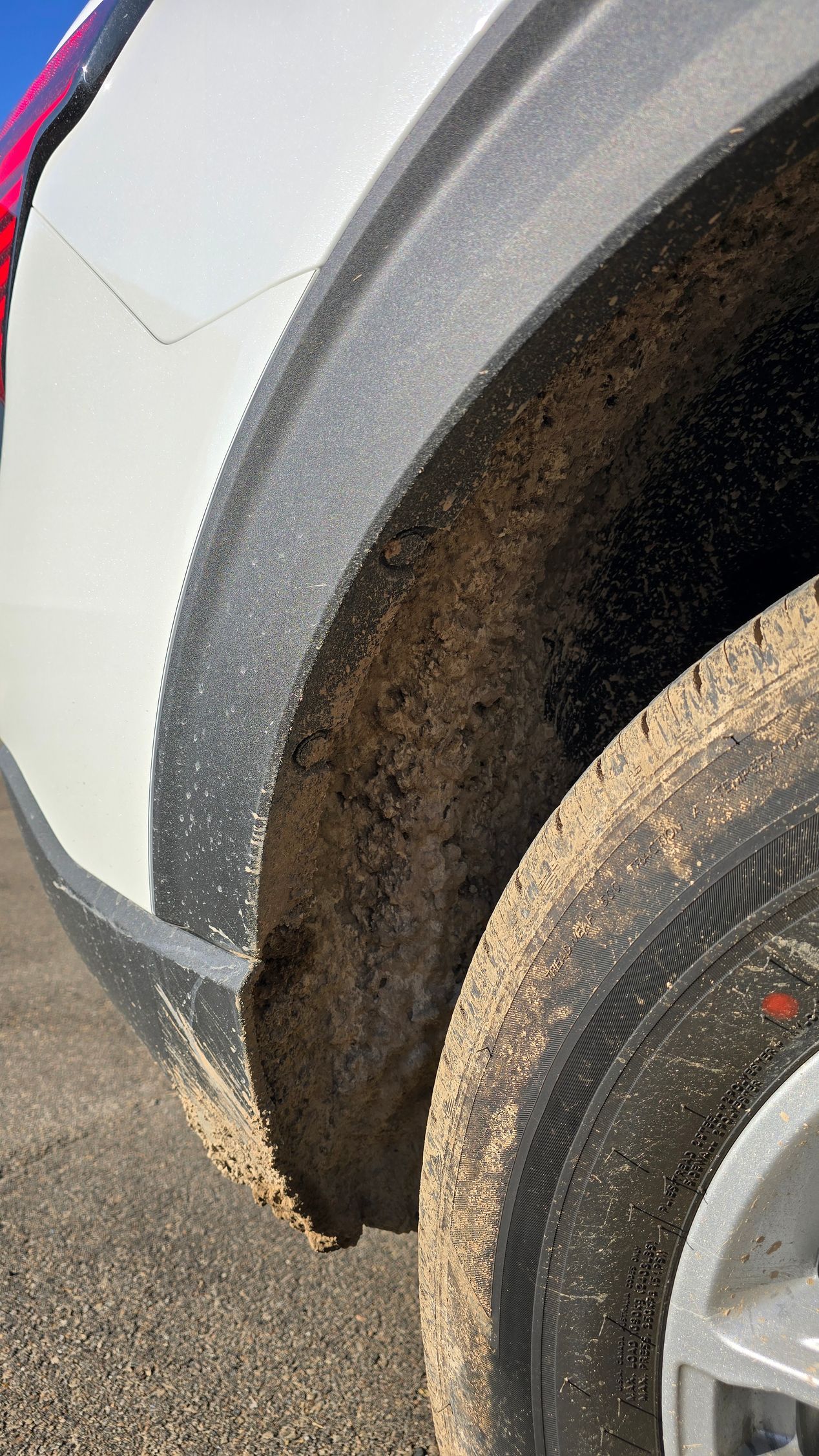 A mud-splattered tire and plastic wheel arch lining on the side of a white vehicle.