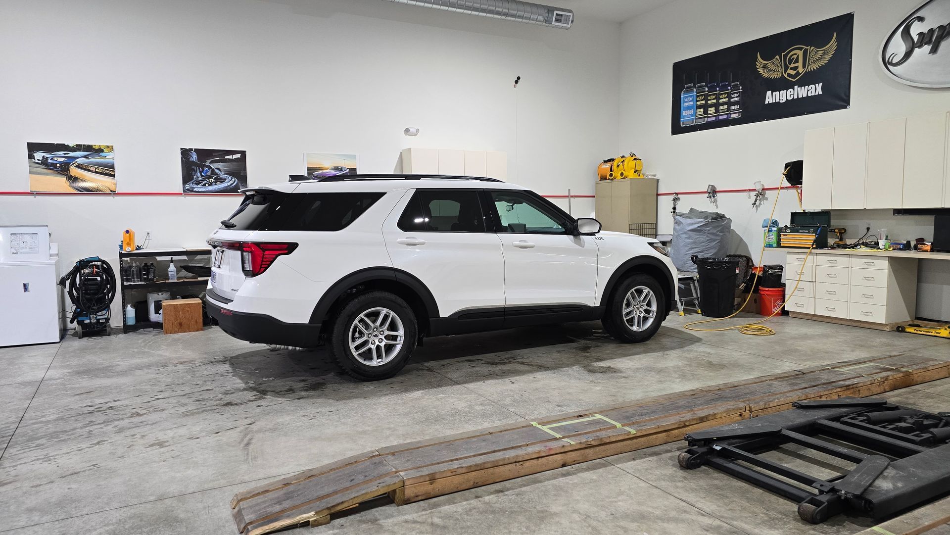 A white Ford Explorer SUV parked inside an auto repair shop with concrete floors, tools, and cabinets visible.