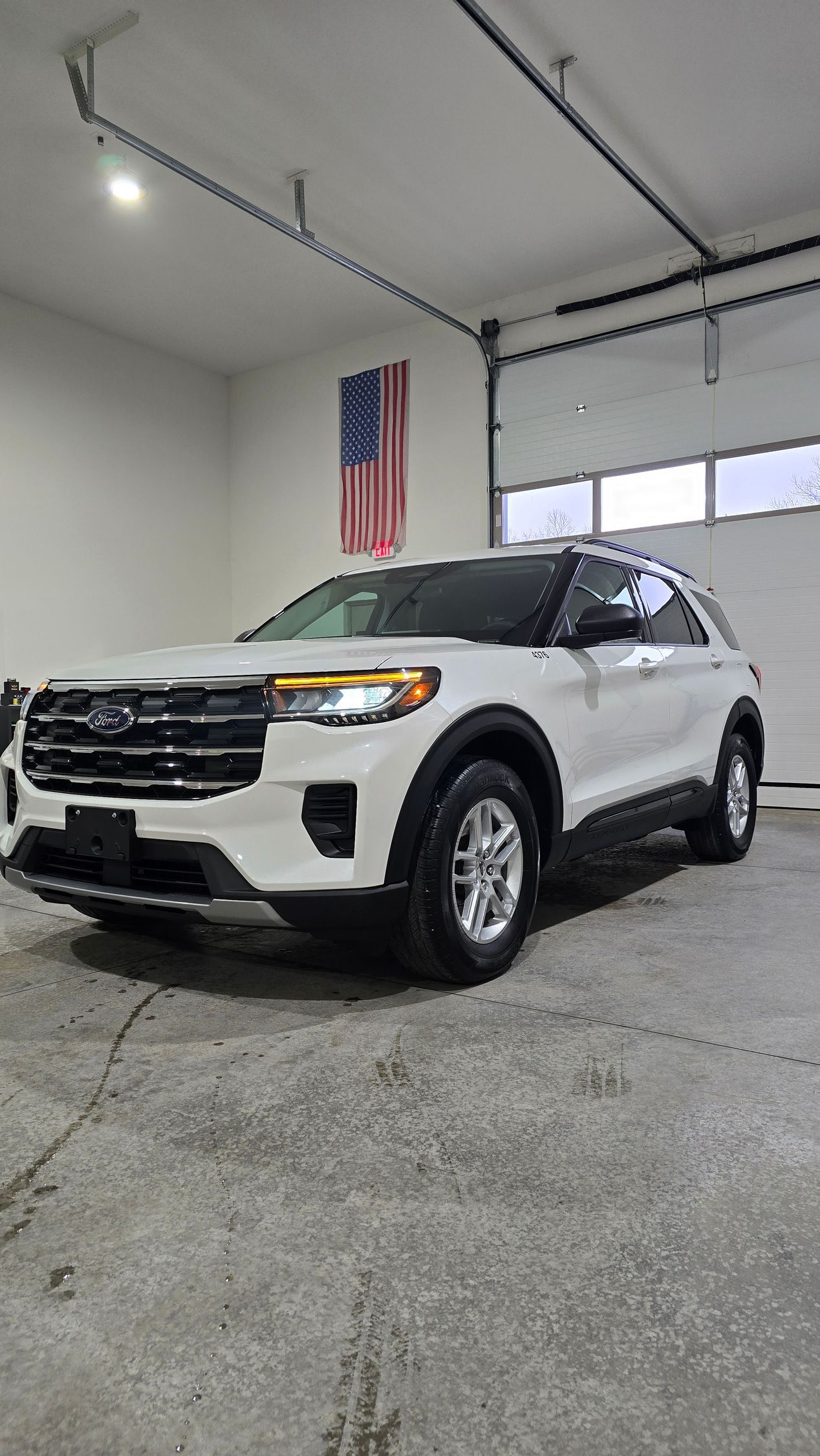 A white Ford Explorer parked inside a garage with an American flag hanging on the back wall.