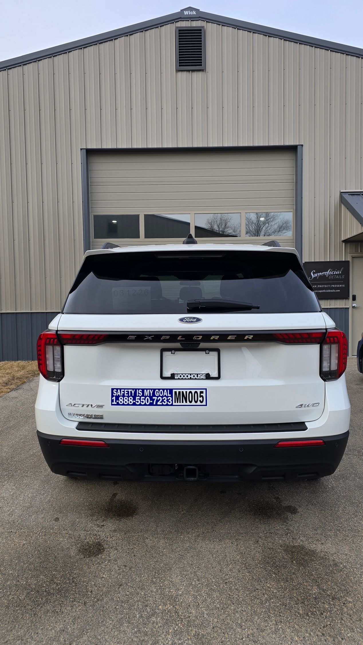 A white SUV parked on gravel in front of a metal industrial garage door.