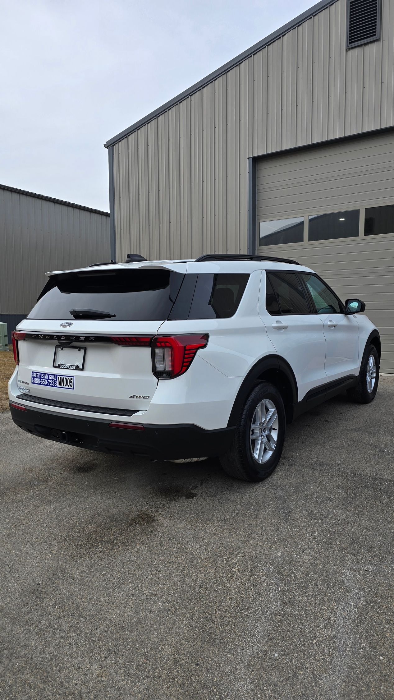 A white Ford Explorer SUV parked on a gravel lot in front of a metal warehouse building.