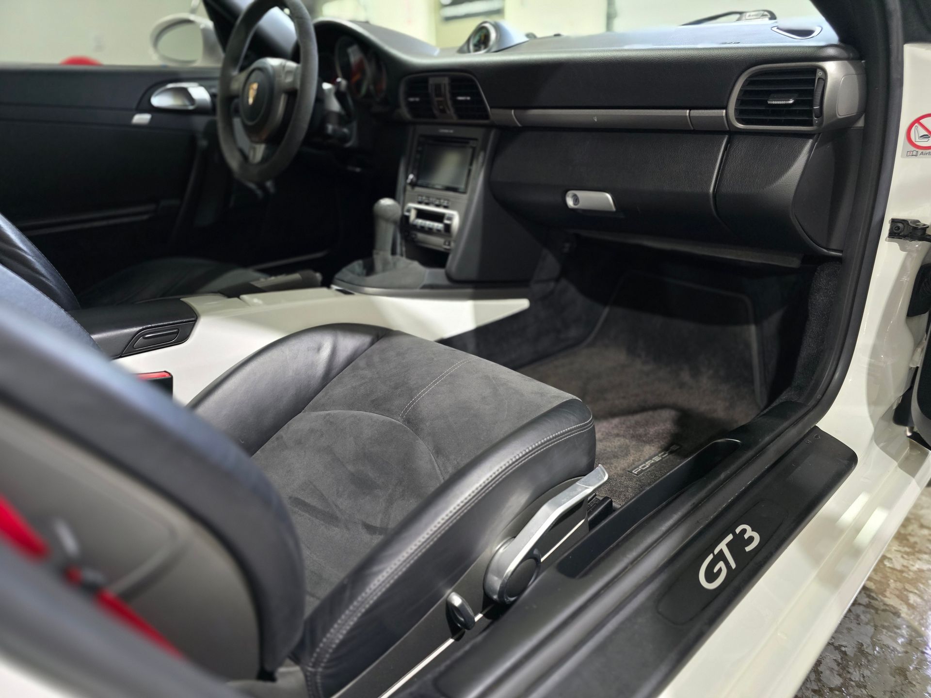 Interior view of a white Porsche GT3, featuring black leather and suede sport seats, dashboard, and branded door sill.