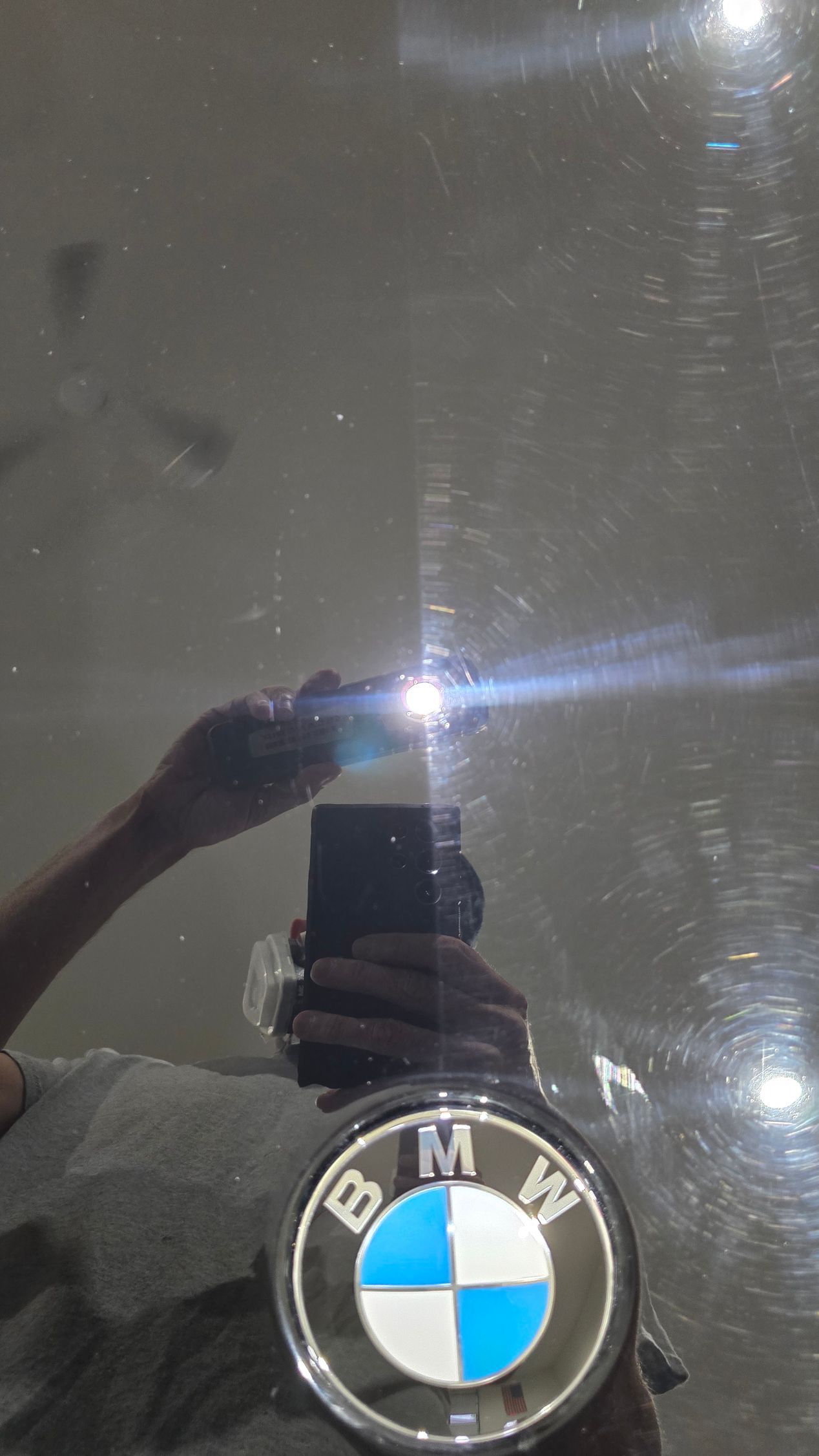Close-up of a BMW emblem on a dark surface, reflecting a hand and light.
