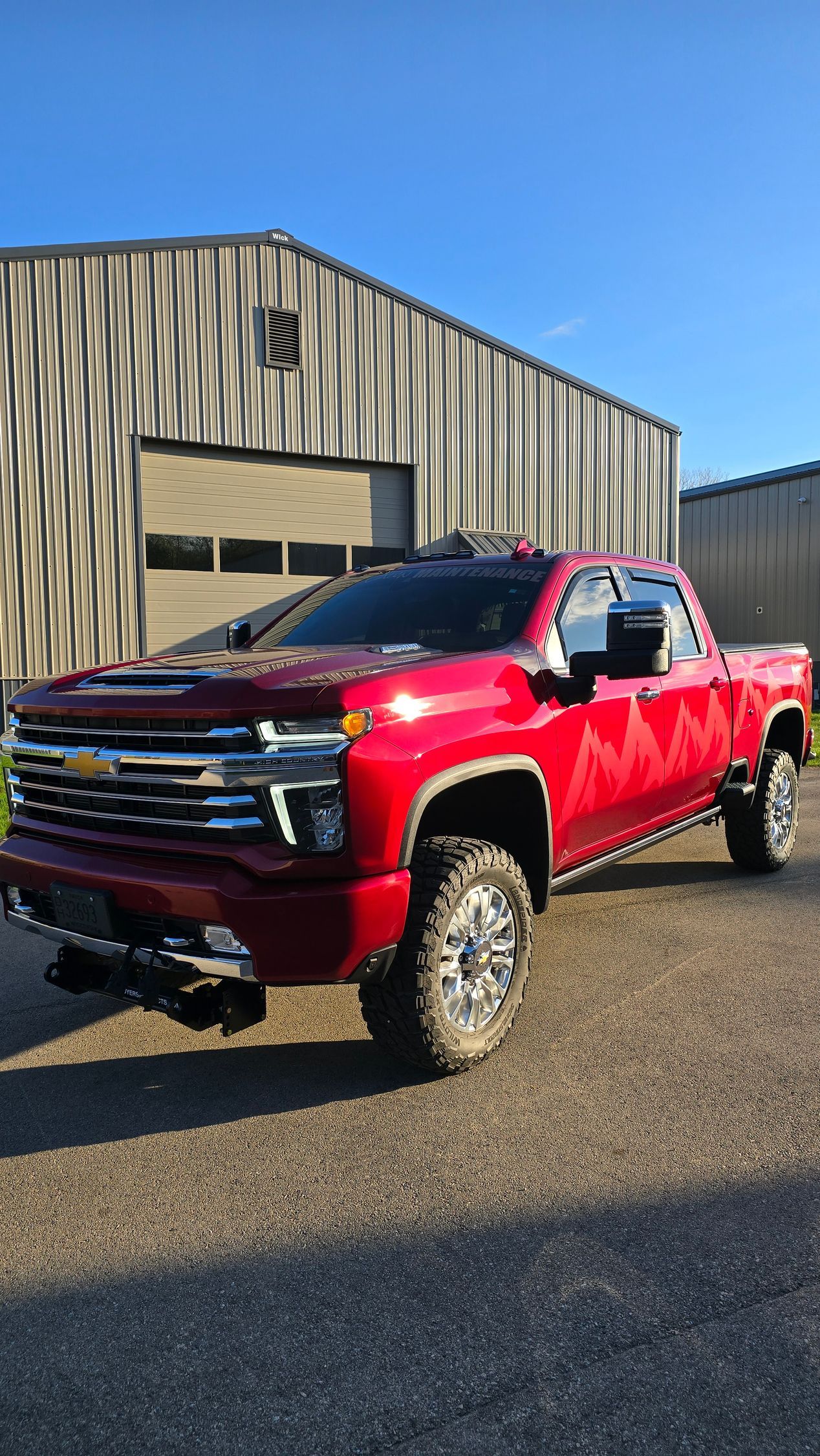 Red Chevy Silverado pickup truck parked outside a corrugated metal building on a sunny day.