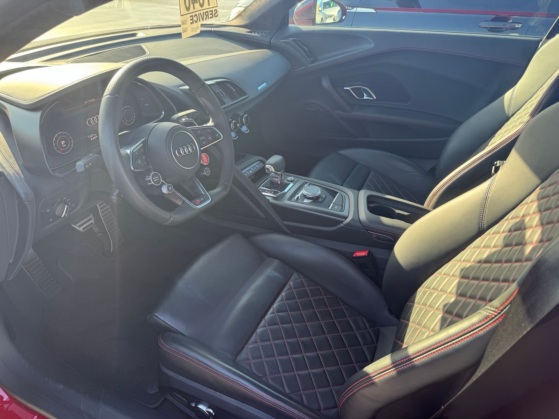 The interior of a modern car with a black leather steering wheel and diamond-stitched black bucket seats with red accents.