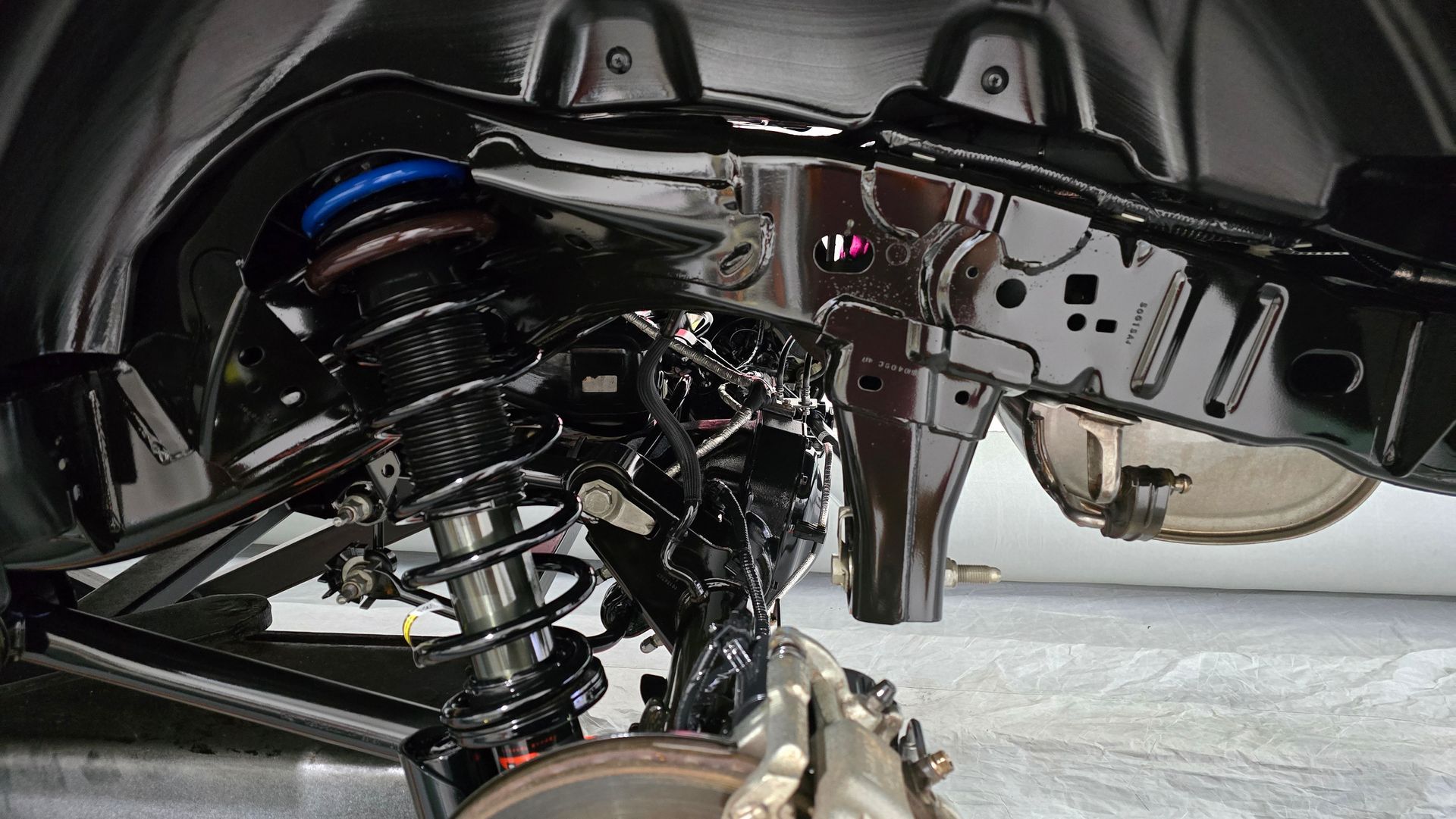 Black car undercarriage with suspension, shock absorber, and frame visible.