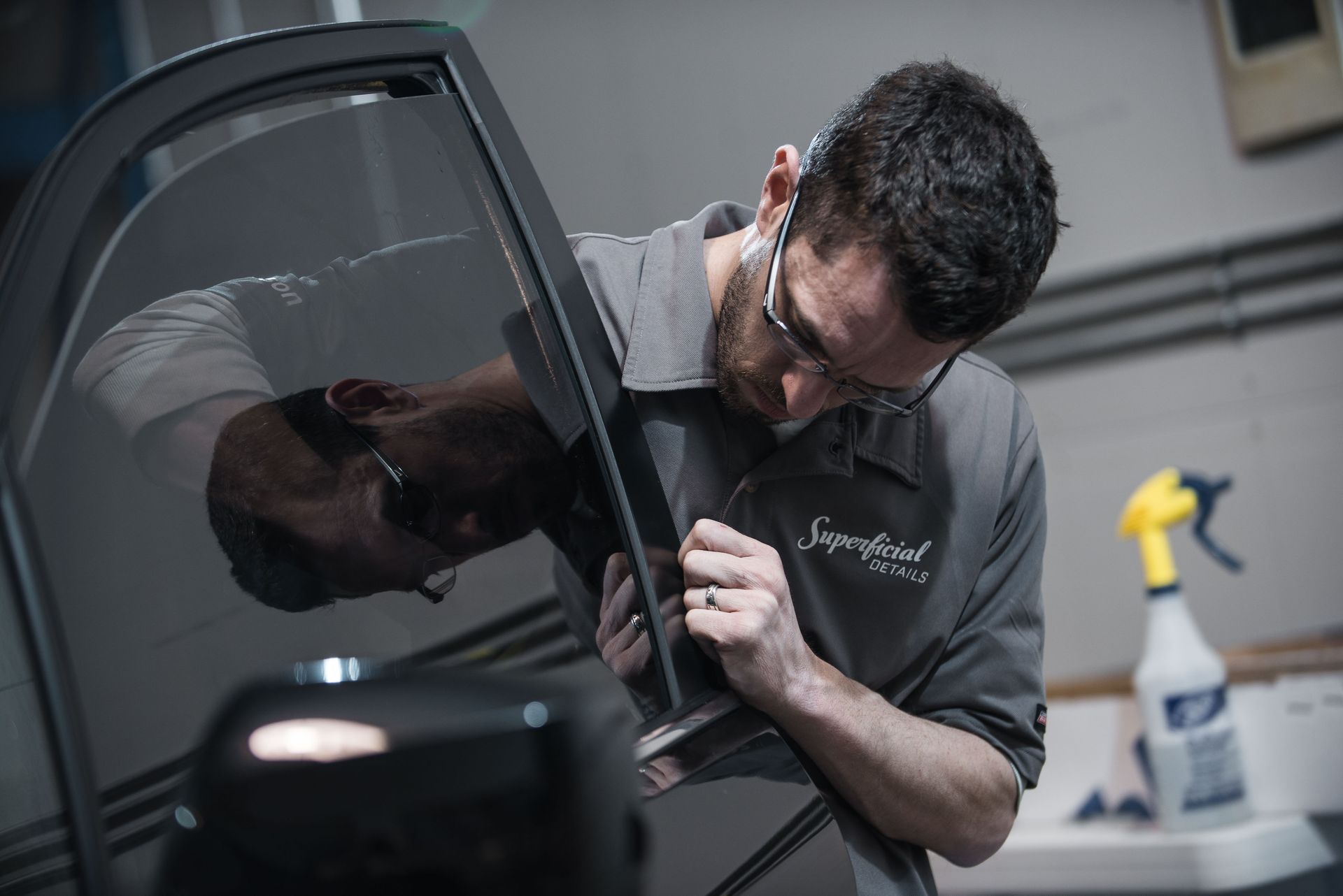 A man wearing glasses is working on a car door.