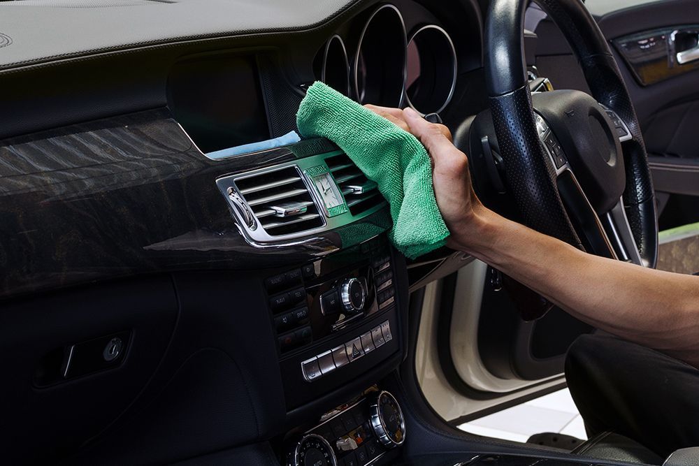 a person is cleaning the dashboard of a car with a green cloth .