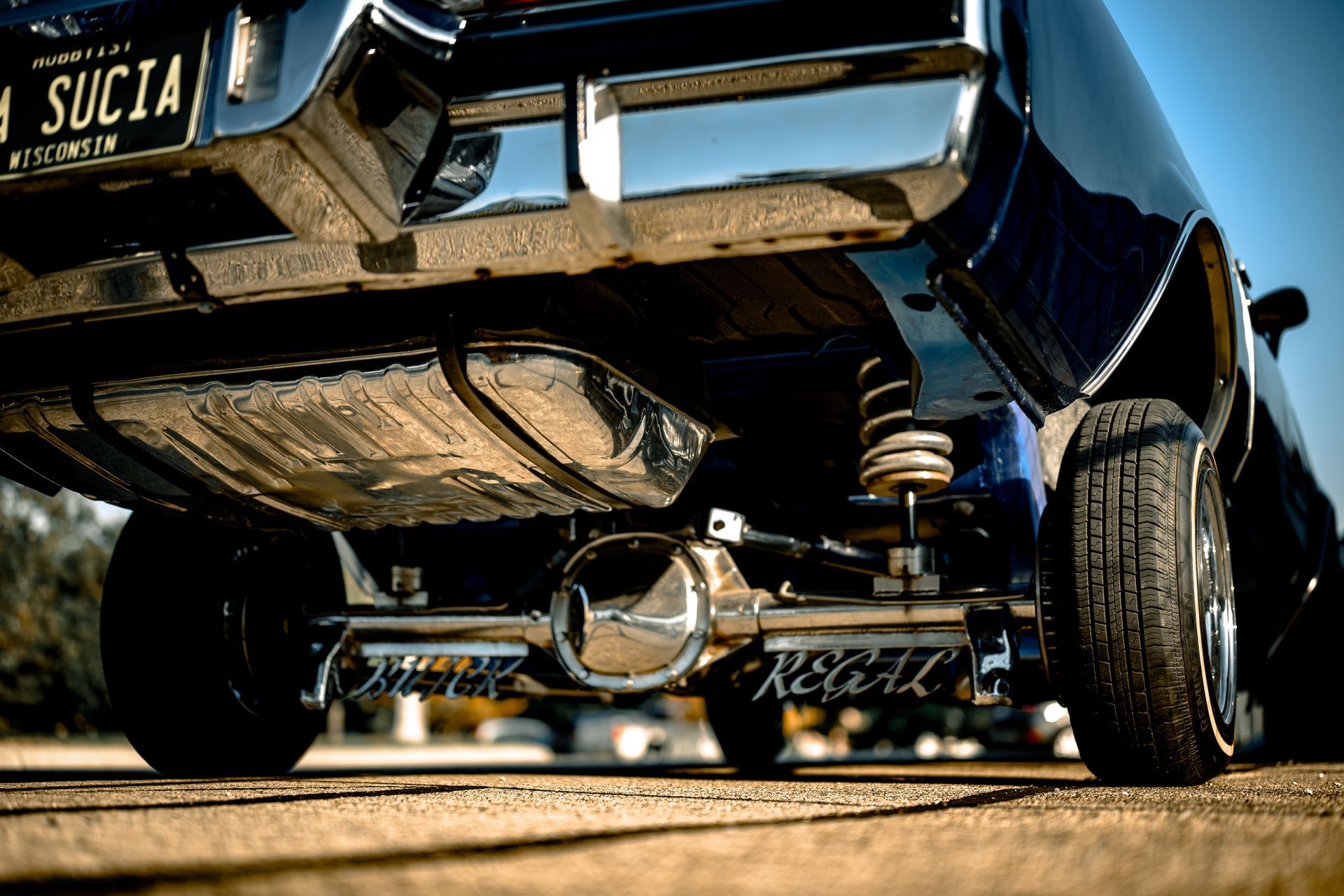 Low-angle view of a lowered black classic car's rear, showcasing suspension, shiny chrome components, and license plate 