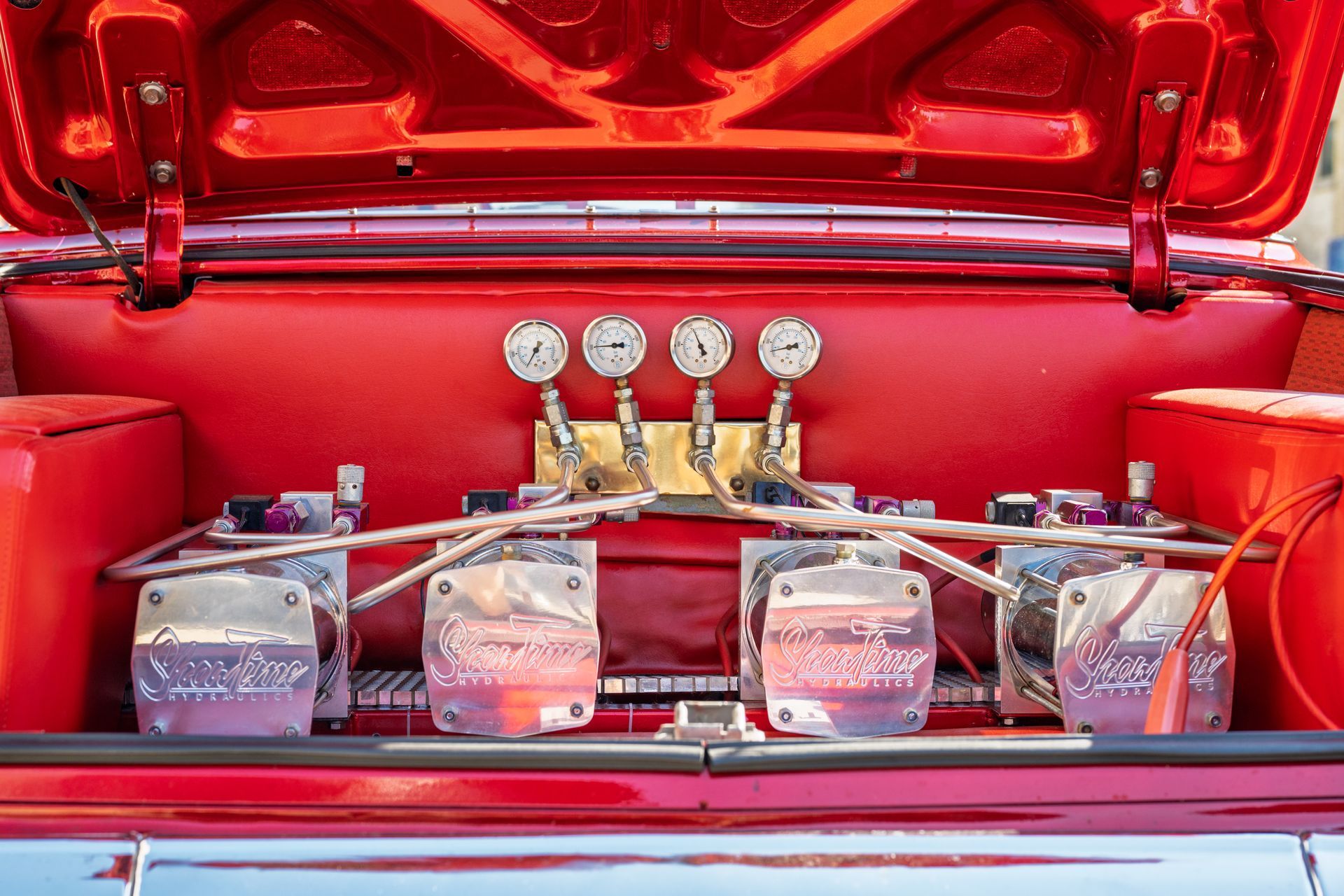 Red car trunk with air suspension system, gauges, and pumps.
