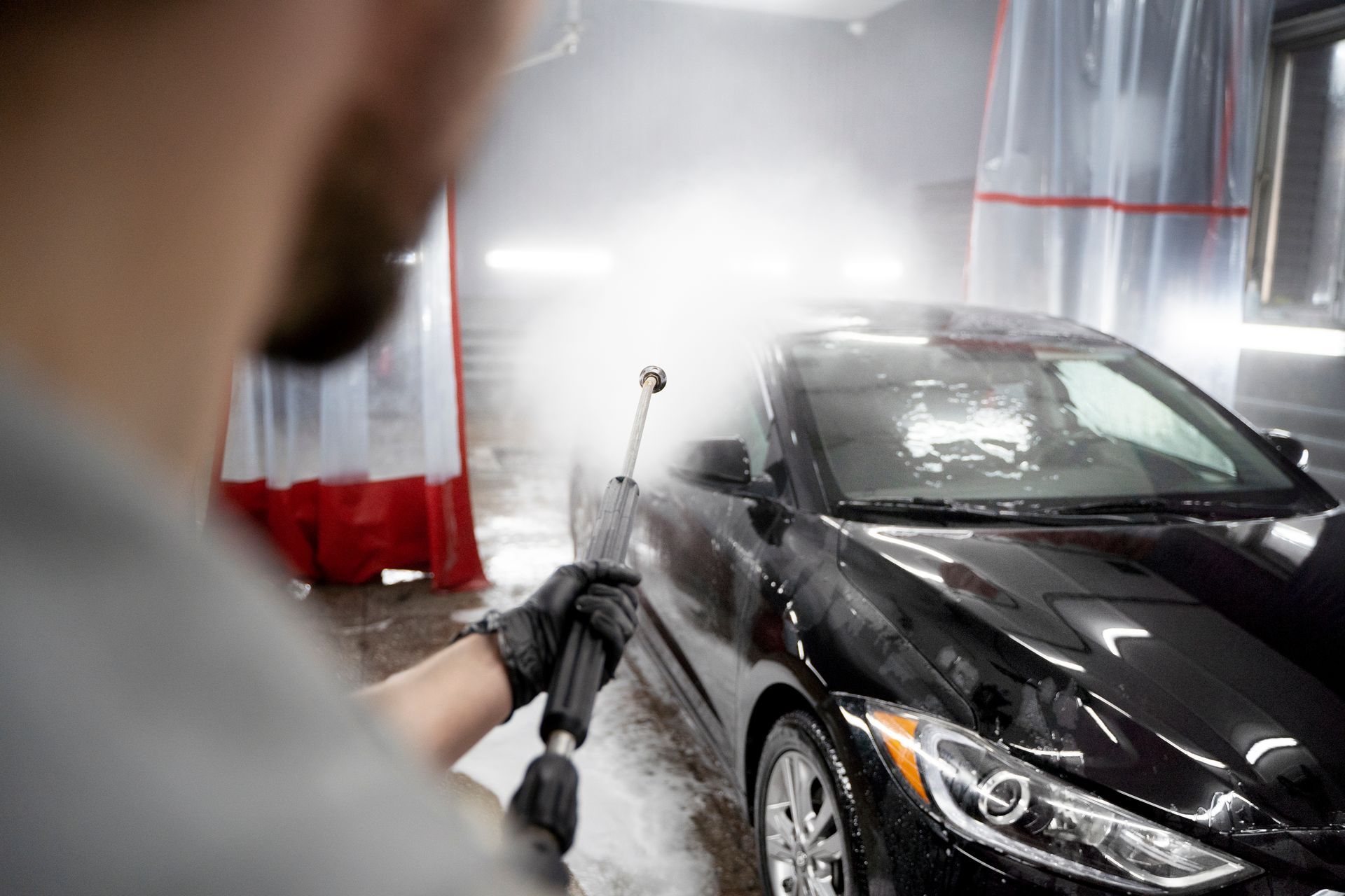 A man is washing a car with a high pressure washer.