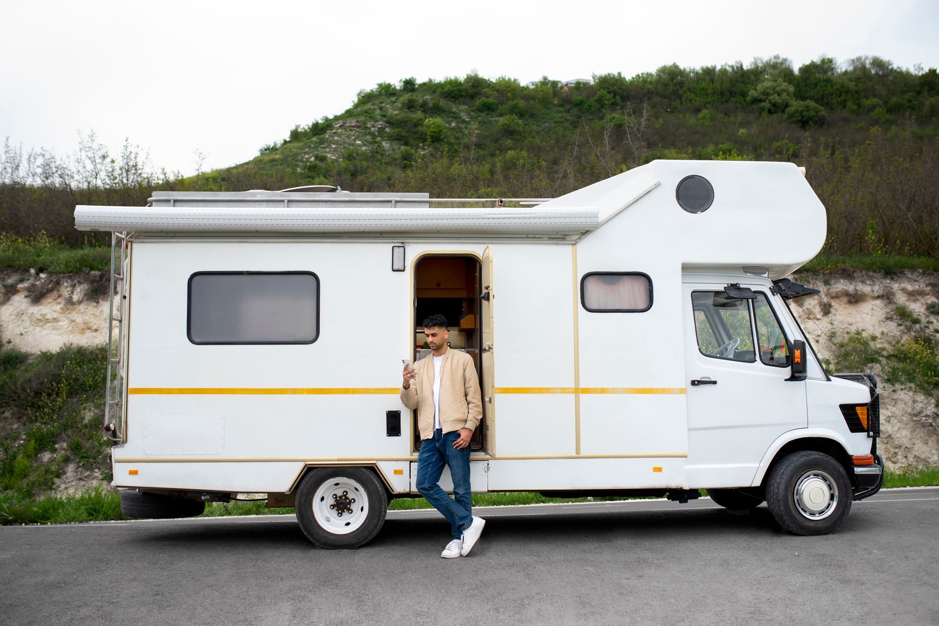 a man is standing next to a white rv on the side of the road .