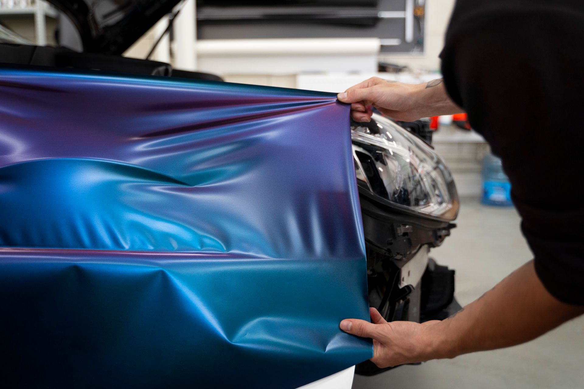 A man is wrapping a car in blue and purple vinyl.