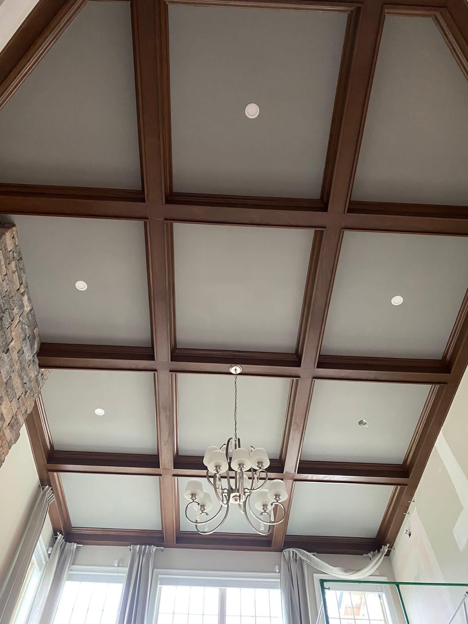 Wooden coffered ceiling with recessed lights, a chandelier, and tall windows with curtains