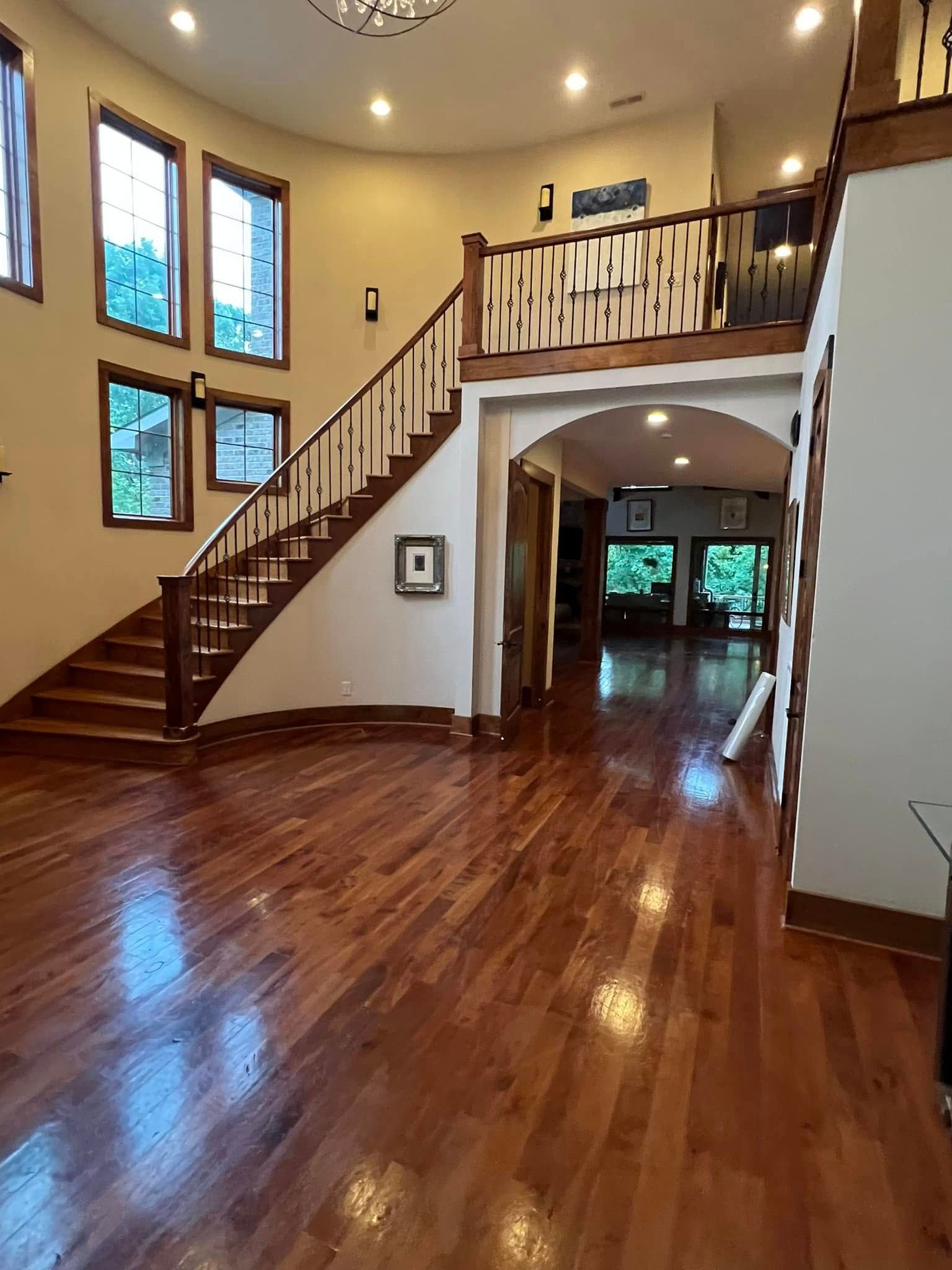 Spacious foyer with polished hardwood floors, curved staircase, arched entry, and tall windows.