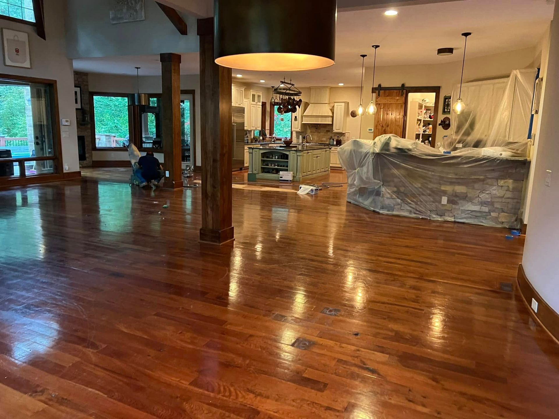 Spacious lobby with polished wooden floor, columns, and furniture wrapped in plastic under warm lighting.