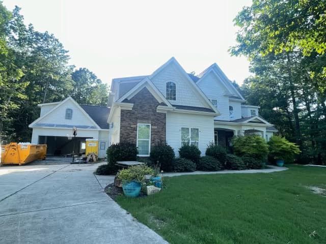 Suburban house with stone facade, driveway, garage, and green lawn surrounded by trees