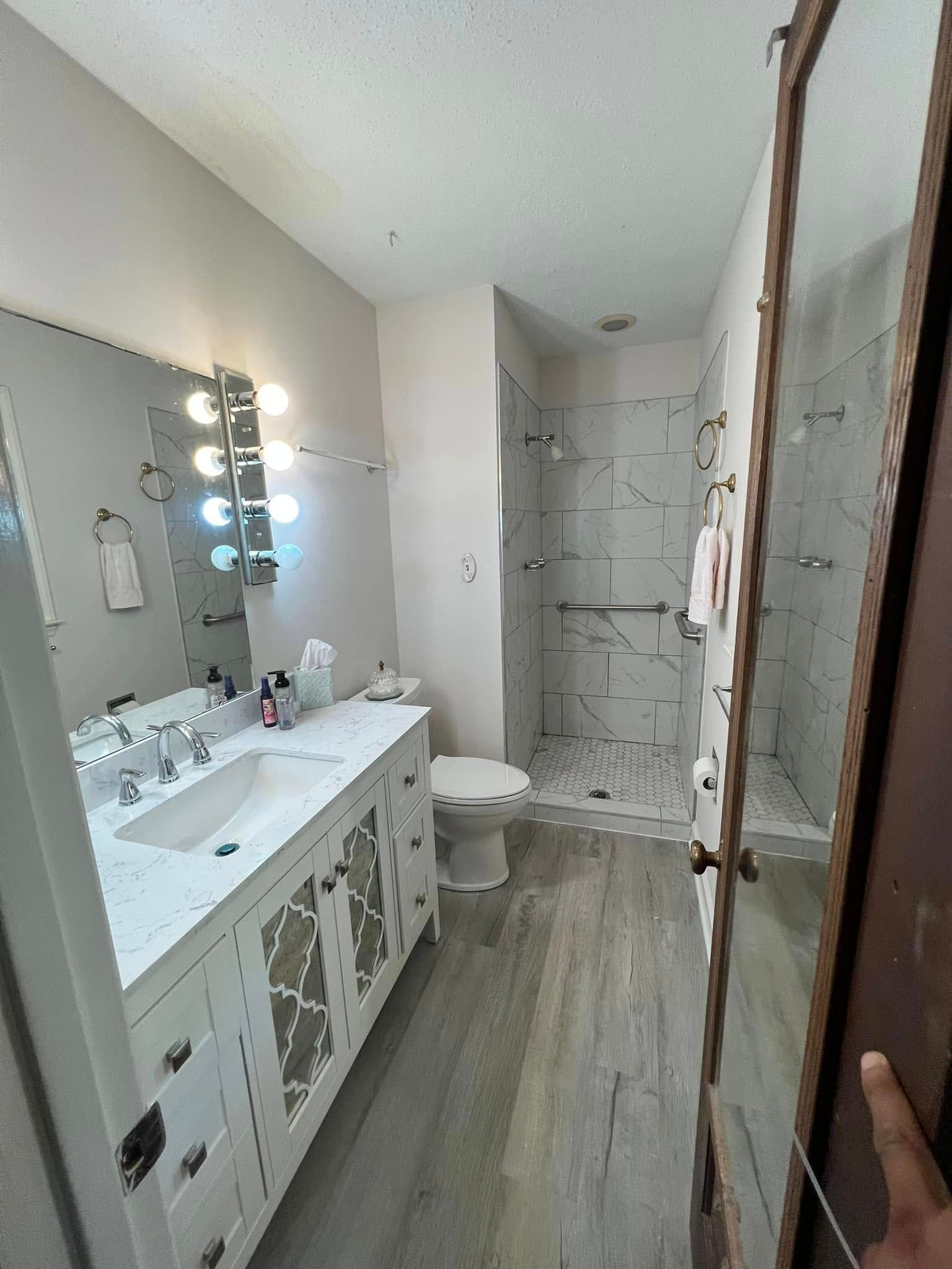 Narrow bathroom with white vanity, lit mirror, toilet, and tiled shower under renovation