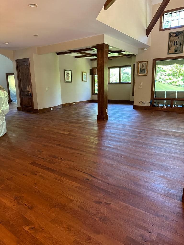 Spacious room with polished wood floors, exposed beams, large windows, and a view of the outdoors