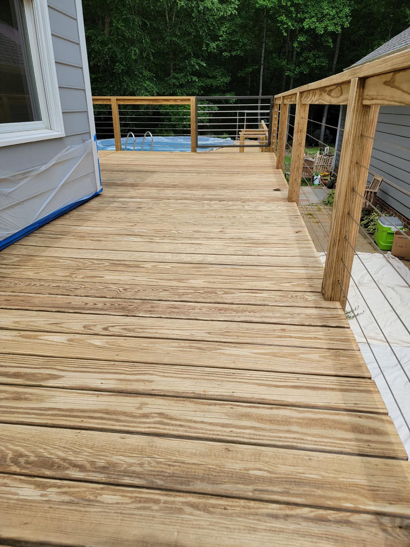 Wooden deck under construction beside a house, with railing and trees in the background.