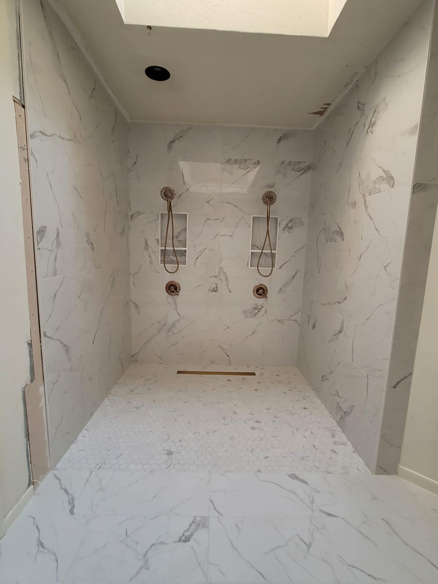 Empty marble-tiled bathroom with a shower niche and ceiling light opening.