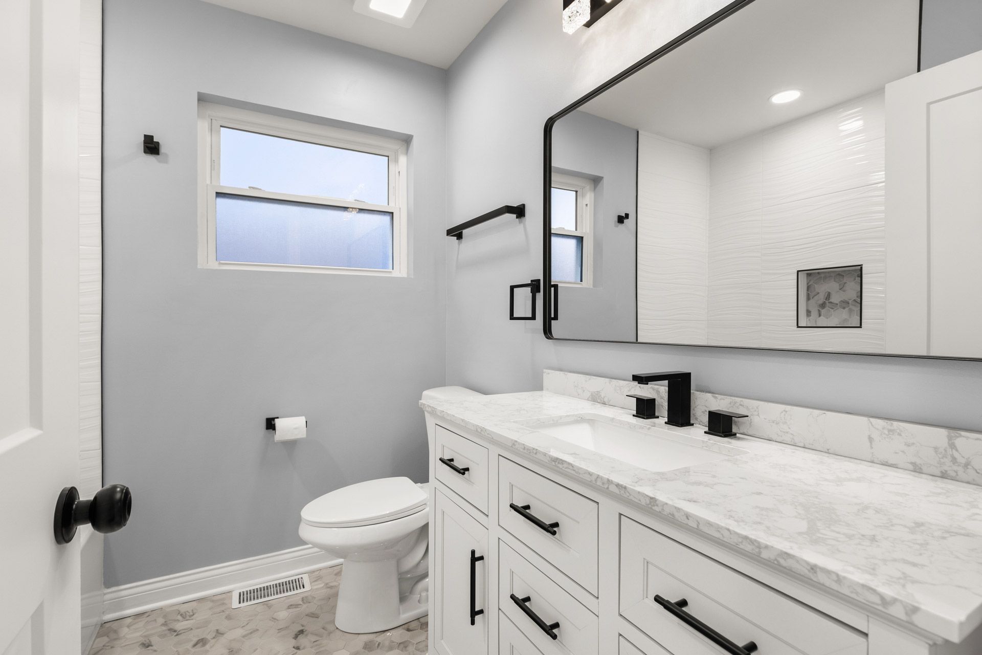 Bright modern bathroom with double vanity, large mirror, toilet, and window on the left.
